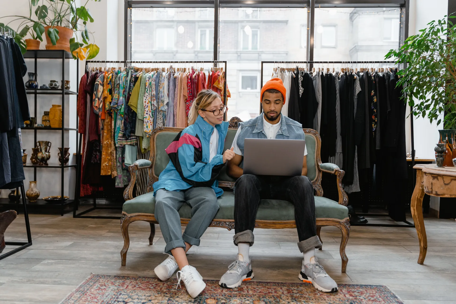 Two people sitting together on a sofa in a clothing shop, working through something on a laptop.